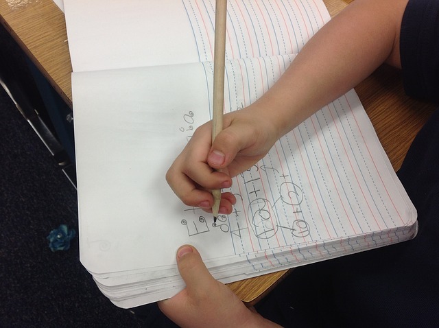 Close-up of hands holding a pencil writing on lined notebook paper, neutral tones, focused mood.